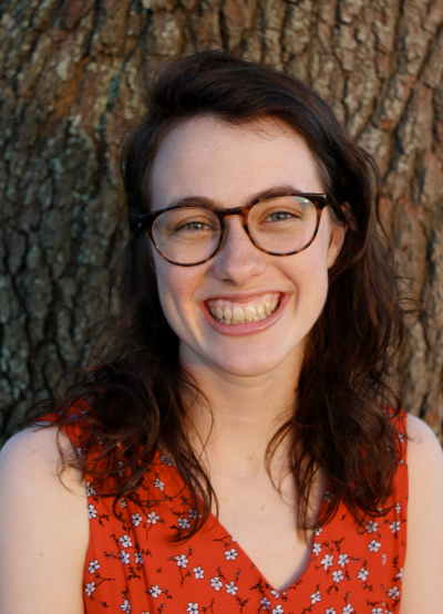 A woman smiling while standing outside in front of a tree trunk