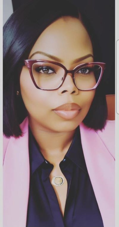 A portrait photo of a woman wearing glasses, a black blouse, and light pink blazer.